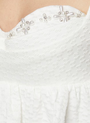 MING MA 在2018年创立了同名品牌，以“An Instinct for Surprise”为理念，运用立体剪裁及垂褶细节打造富雕塑感的服饰。这款上衣凭借流畅利落的剪裁打造出蓬松下摆的版型，珍珠水钻缀饰衬于提花面料之上，为单品增添丝丝精致气息，结合干净优雅的白色调，一展你优雅魅力。展示图